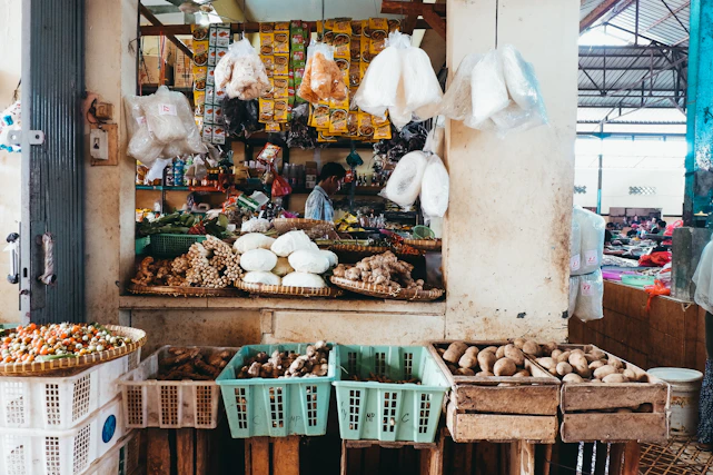 A vibrant market stall showcasing bundles of fresh garlic, ginger roots, and coconuts under warm sunlight.