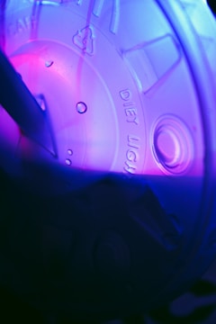 A close-up view of a translucent plastic lid with the words 'diet light' stamped on it. The lid is illuminated by pink and purple lighting, creating a vibrant and abstract visual effect. Water droplets are visible on the surface, adding texture and interest to the composition.