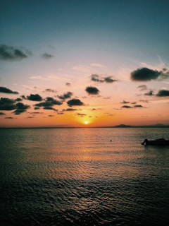 Golden sunset over the calm sea with a silhouette of a boat near Tropea coastline.