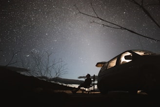 A foldable outdoor camping chair set up beside a campfire under a starry night sky.