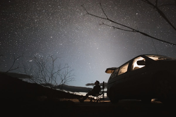 A foldable outdoor camping chair set up beside a campfire under a starry night sky.