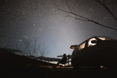 A lightweight camping chair set up beside a glowing campfire under a starry night sky.
