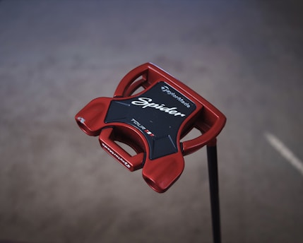 A red golf putter head with a modern shape, featuring the brand name TaylorMade and the model name Spider written on it. The putter has a glossy finish and is designed with a mix of sharp and smooth edges for improved performance.