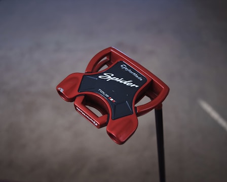 A red golf putter head with a modern shape, featuring the brand name TaylorMade and the model name Spider written on it. The putter has a glossy finish and is designed with a mix of sharp and smooth edges for improved performance.