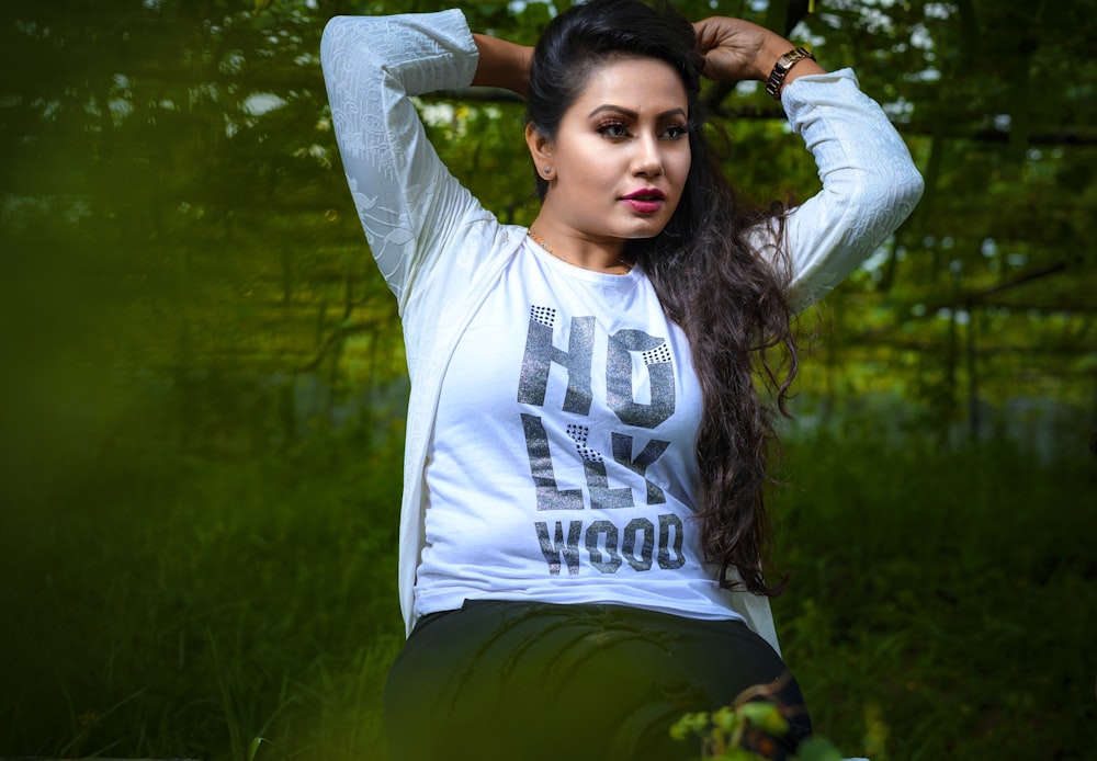 woman wearing white and black crew-neck top sitting on grass fields