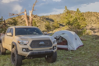 A rugged white pickup truck loaded with camping gear against a forest backdrop.