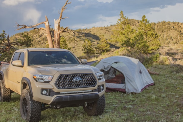 A rugged white pickup truck loaded with camping gear against a forest backdrop.