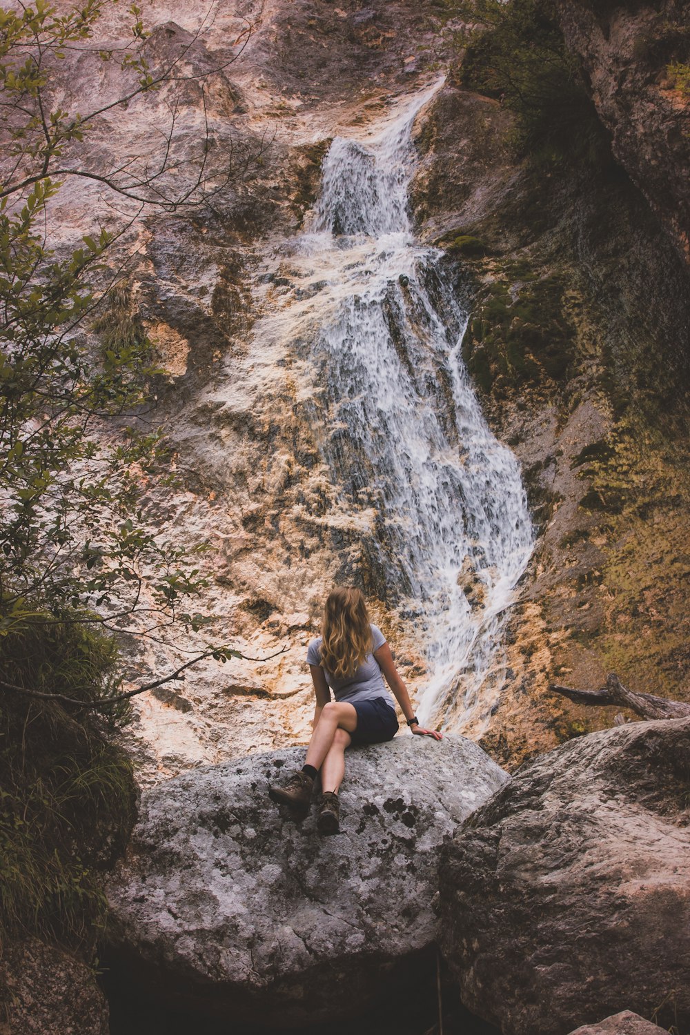 woman sitting on rock near waterfalls