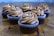 Six chocolate cupcakes topped with swirled chocolate frosting and chocolate chips are arranged on a wooden surface. The cupcakes are in brown liners with a textured appearance. The background is softly blurred, highlighting the focus on the cupcakes.