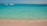 A serene beach with turquoise waters and a fast boat anchored nearby under a clear sky.