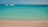 A serene beach with turquoise waters and a fast boat anchored nearby under a clear sky.