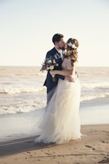 bride and groom standing beside shoreline