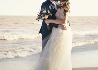 bride and groom standing beside shoreline