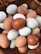 A wicker basket filled with a variety of farm eggs, displaying a range of colors from white to deep brown, including some pale green and blue hues. The eggs are different sizes and textures, lying closely together, creating a natural and rustic appearance.
