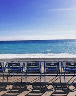 a row of blue chairs sitting on top of a sandy beach