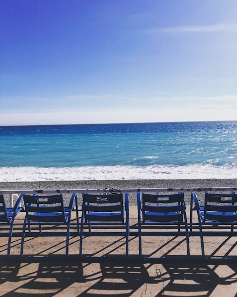 a row of blue chairs sitting on top of a sandy beach