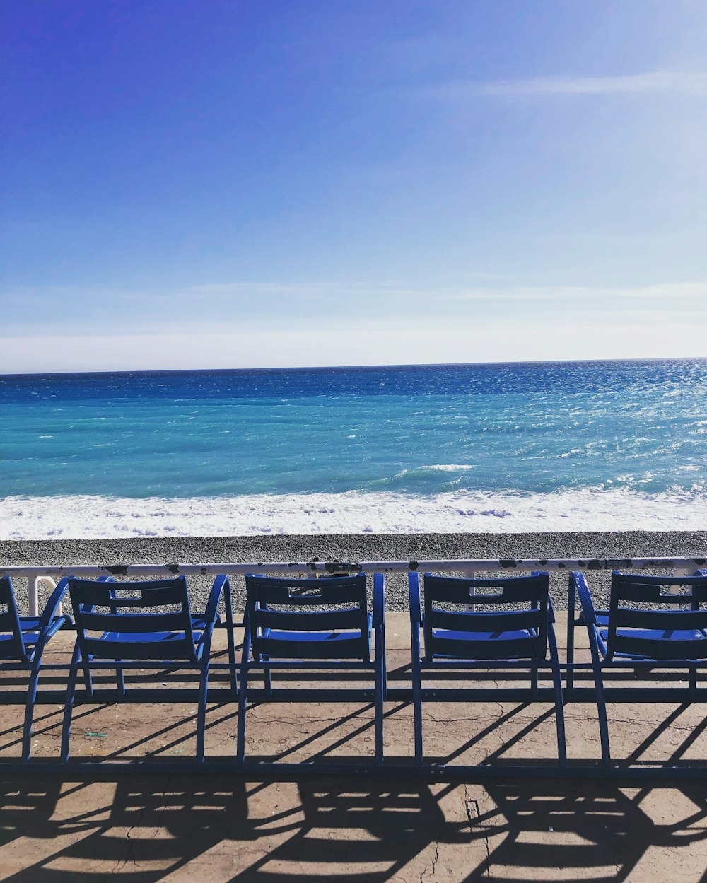 a row of blue chairs sitting on top of a sandy beach