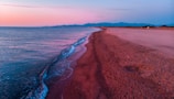 A pristine beach at sunset with soft waves and a purple-hued sky.