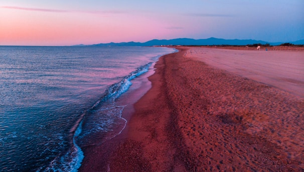 A serene Australian beach at sunset with soft waves and golden sand stretching under a colorful sky.