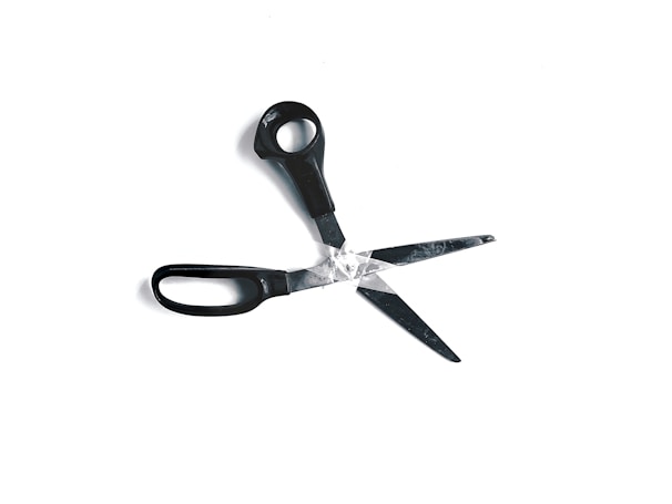 A pair of black-handled scissors has one blade broken off, with the two blades overlapping slightly against a white background.
