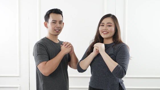 An elegant Asian woman smiling warmly, standing beside a Caucasian man in a softly lit, modern setting.