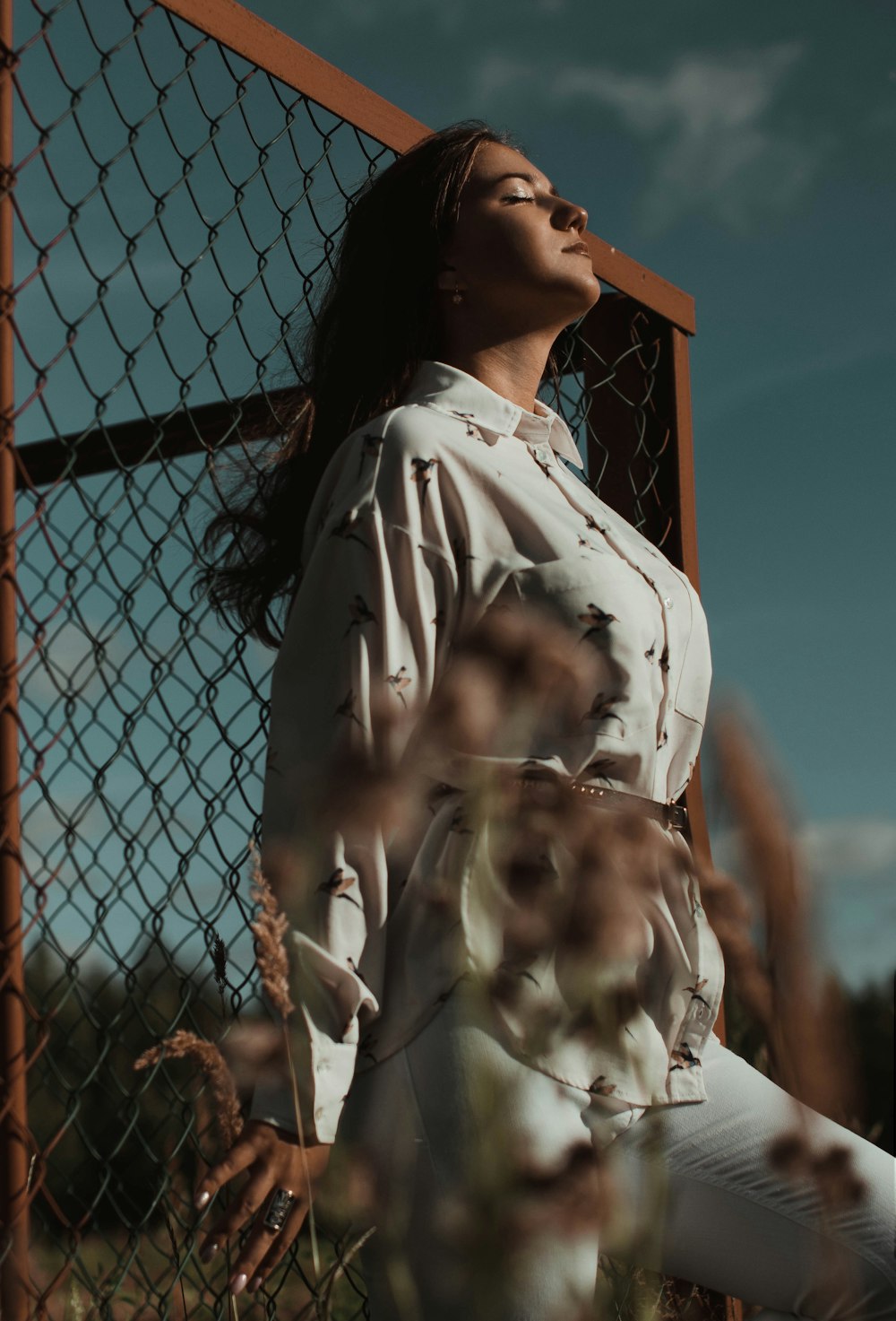 woman wearing white blouse leaning on fence