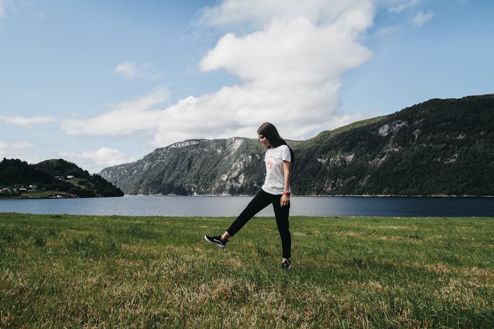 woman walking on grass field beside body of water