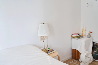 A minimalist bedroom corner featuring a simple white nightstand with a small stack of books and a candle