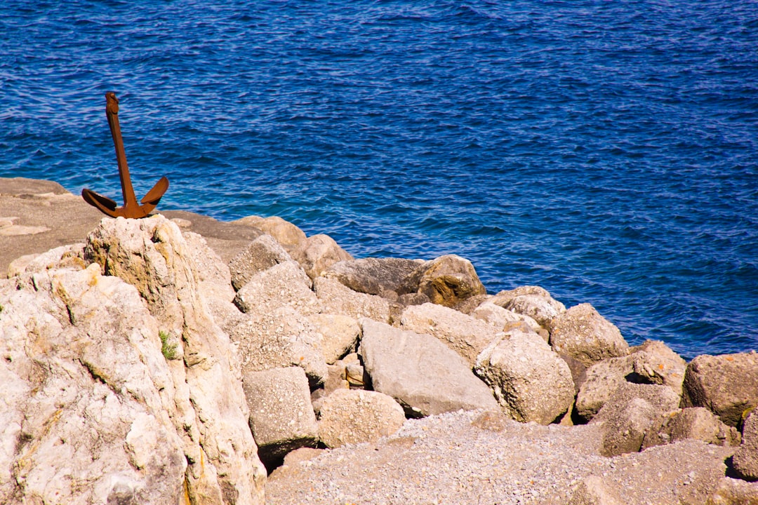 brown rock formation near body of water, An anchor laying on rocks on the Amalfi coast along the blue ocean and water.