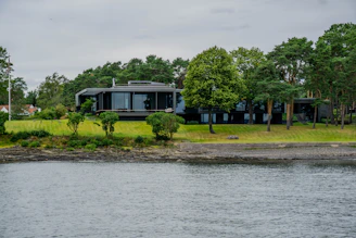A stunning modern luxury home with large glass windows overlooking a serene waterfront at sunset.