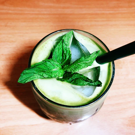 Refreshing glass of green cold pressed juice with mint leaves and cucumber slices.