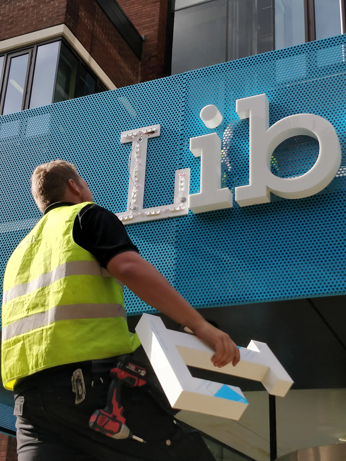 Installer in a hi-vis vest at a large sign panel