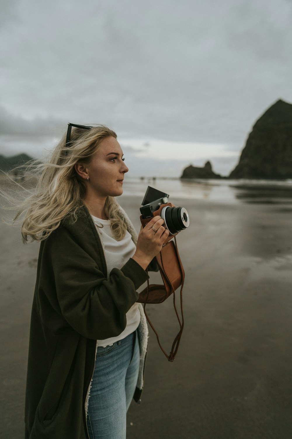 a woman standing on top of a beach holding a camera