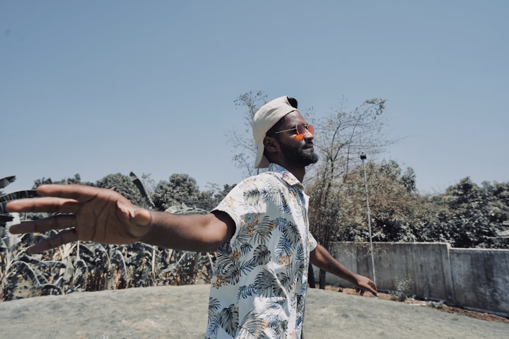 man in white red and blue floral shirt and white cap standing on brown field during