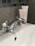 A chrome faucet mounted on a white porcelain sink, with a hint of a tiled wall in the background. Two tubes of skincare products are partially visible, positioned behind the faucet.