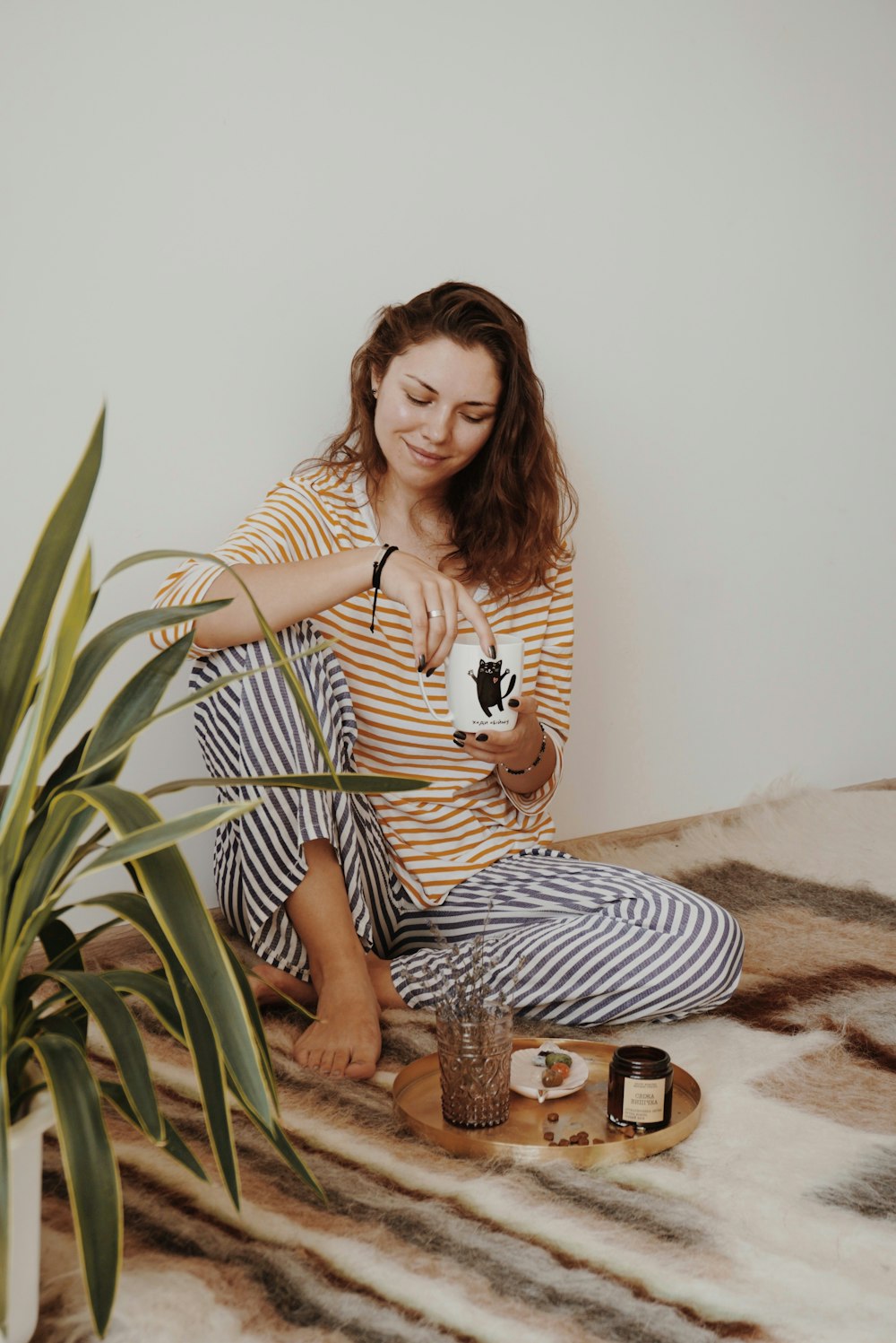 woman wearing yellow and white stripe long-sleeved shirt holding white ceramic mug