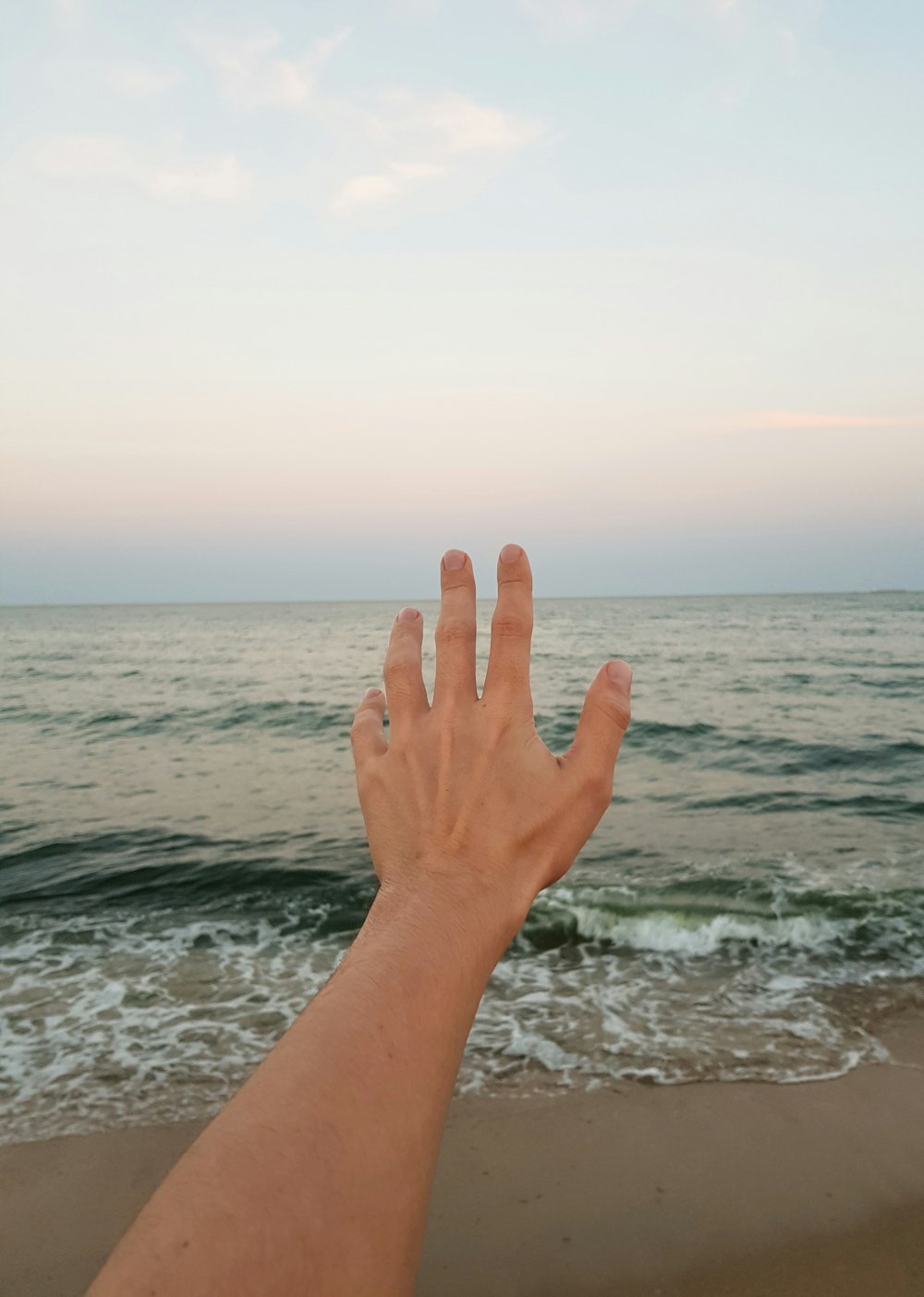 a person's hand reaching out towards the ocean