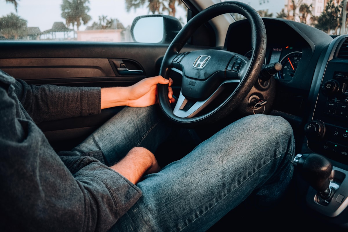 Person gripping a car steering wheel while driving on a highway