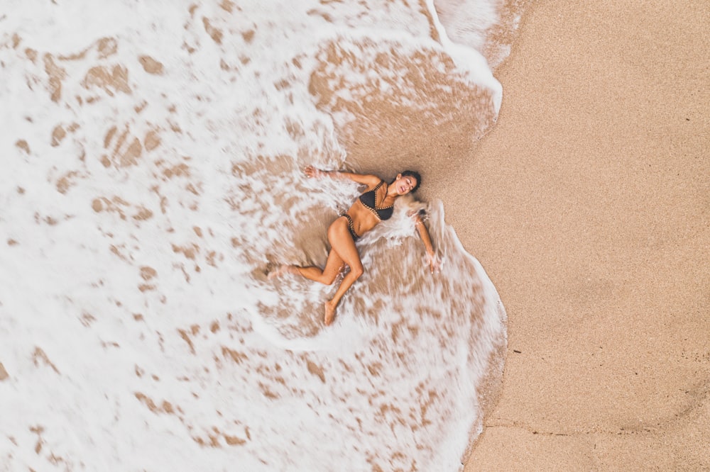 a woman laying on top of a sandy beach next to the ocean