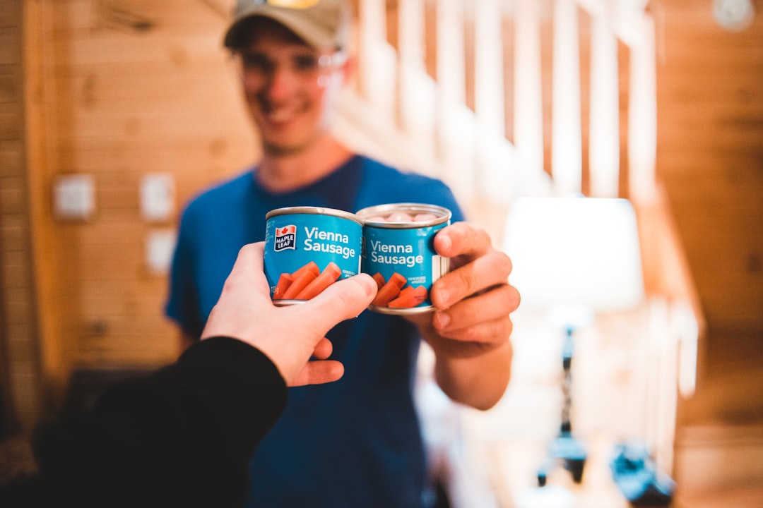 two person holding Vienna sausage cans