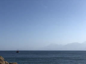 A calm sea with a ship sailing towards the horizon under a clear sky.