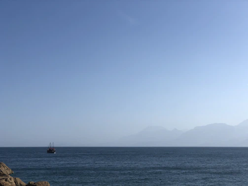 A calm sea with a ship sailing towards the horizon under a clear sky.