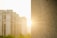 A textured concrete wall is in sharp focus on the right, while the background shows blurry, multi-story apartment buildings illuminated by the soft glow of sunlight.
