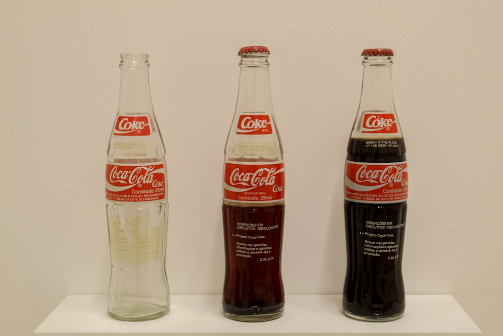 three bottles of coke on a white shelf