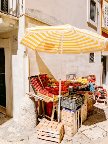 A cozy small fruit and vegetable stand with fresh produce displayed under a sunny sky.