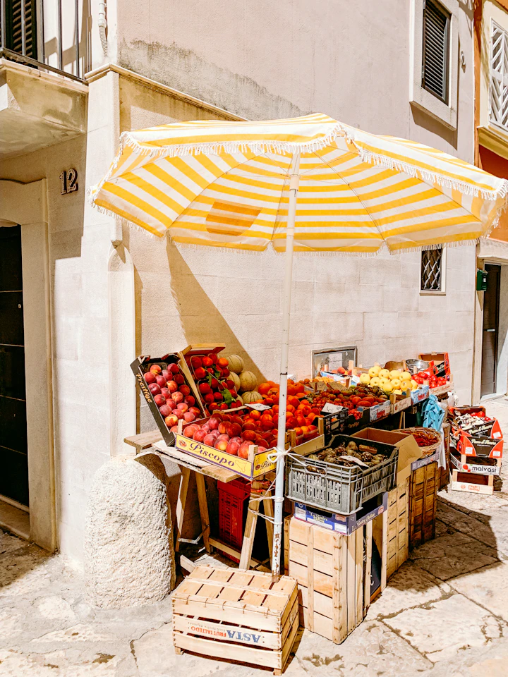A street produce stall under a striped umbrella