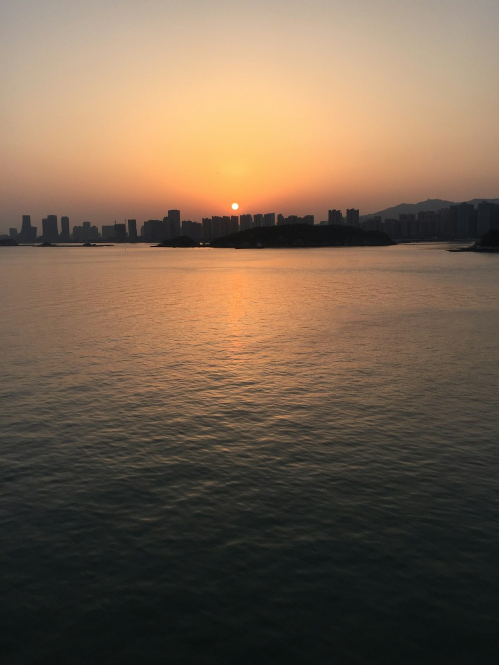 Cuerpo de agua tranquilo cerca de los edificios de la ciudad bajo el cielo naranja