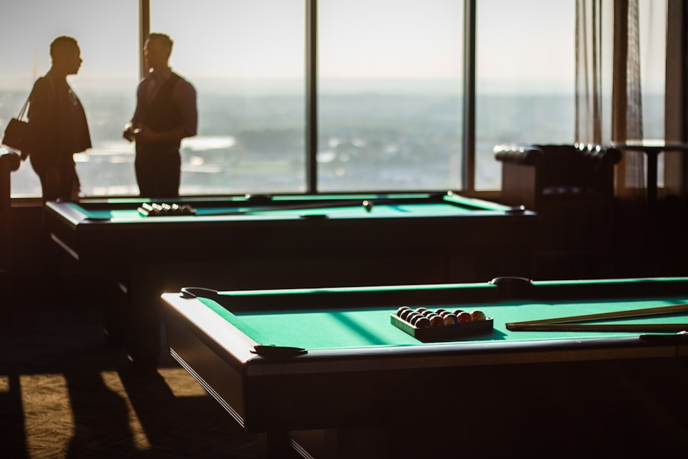 Deux hommes discutent à côté d’une vitre près de deux tables de billard