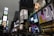 Bright electronic billboards and advertisements illuminate the bustling urban environment in an area crowded with vehicles and people. The signs include various brands, and the scene captures the vibrancy and energy of a commercial hub.