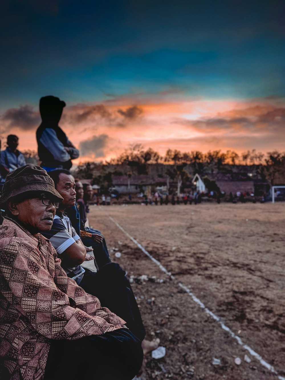 man in black and white checkered dress shirt sitting on ground during sunset